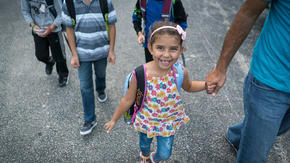 Jori holds her father's hand while walking to school