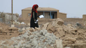 A woman picks her way through the rubble of her village in Northeast Syria.