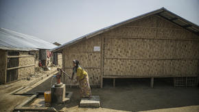 A Rohingya women pumps water outside a longhouse in Myanmar