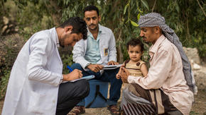 A health workers writes notes as he examines a child sitting on his father's lap