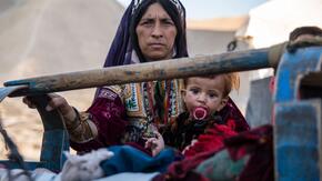 A mother rocks her sick child, who has a pacifier,  in a camp in Badghis  
