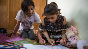 Two Yazidi sisters in Sinjar, Iraq sit on the floor of their home, coloring