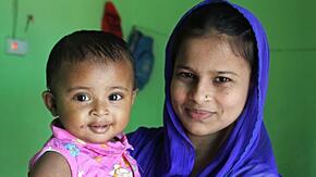 Lovely Akter, an IRC midwife, poses with her nine-month-old daughter. Lovely is wearing a blue headscarf and her daughter is wearing a pink shirt. Both are smiling. 
