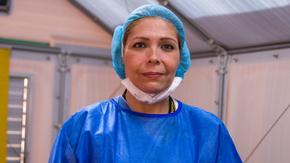 Dr. Edna, an IRC doctor from Venezuela working in Colombia, is inside a medical tent and wearing bright blue scrubs. She is looking straight at the camera. 