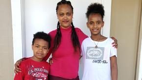 Abrehet stands with her arms around her children Kudus, 5, and Delina, 8, outside their home.