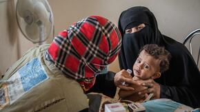 An IRC health worker examines a child in Yemen for malnutrition as his mother holds him in her arms.