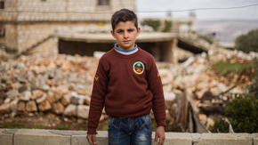 Ten-year-old Ali stands in front of his family's home which was damaged by an airstrike. 