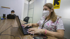 An IRC healthworker wearing a mask to protect herself from COVID-19 types at a laptop