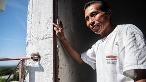 Reynaldo, a Salvadoran man who works as a painter, stands in the doorway of a church in El Salvador.