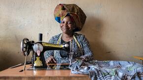 Domitila Kaliya, a Congolese refugee, smiles as she sits at her sewing machine