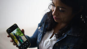 Rosa, wearing a jean jacket, holds an smart phone to show a photo of her daughter, Emily. 