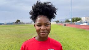 Wearing a red shirt and smiling, Kezia looks at the camera while on a soccer field 