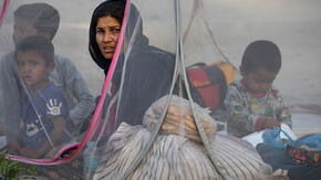 An Afghan mother sits in a tent with her young boys at a makeshift IDP camp. 