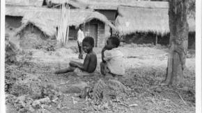 Angolan refugee children sit on the ground outside a row of houses in Zaire.