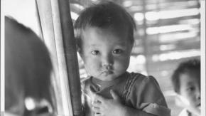 A young girl from Southeast Asia looks at the camera with a serious expression.