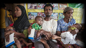 Surrounded by other waiting families, a man holds a young child he has brought to an IRC health center in Myanmar for treatment.