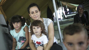 A Syrian refugee woman sits with her son and other family members inside a tent.