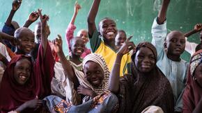 Smiling children eagerly raise their hands in a classroom in Nigeria