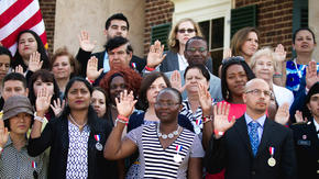 Group of people resettled in the U.S. stand together and raise their right hands as they are sworn in as citizens.