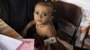 A small child being examined at an IRC clinic in Yemen has her upper arm measured with a MUAC tape, which shows she may be acutely malnourished.