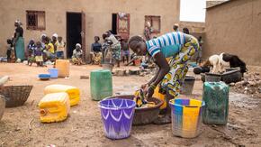 A girl washes clothes as families stand outside a school used as a shelter for Internally Displaced People (IDP) from northern Burkina Faso on June 13, 2019 in Ouagadougou.