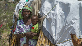 A displaced mother, smiling, holds her baby boy outside a makeshift tent in northern Cameroon.
