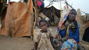Sudanese refugee woman and girl sitting outside a shelter made of blankets and sheets.