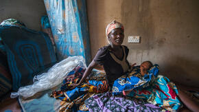 A Nigerian woman sits on a mattress with her infant child. 