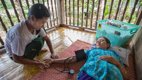 An IRC health worker takes the blood pressure of a female patient lying on a mat on the floor in Thailand.