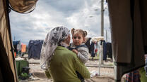 A mother holds her toddler daughter and looks out from their tent on a cloudy day in a refugee camp in Idomeni, Greece.