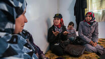 An IRC staff member checks in with a Syrian refugee woman and her family in Zaatari refugee camp in Jordan. An IRC staff member talks with a Syrian refugee family seated on cushions in their shelter in Zaatari refugee camp in Jordan.