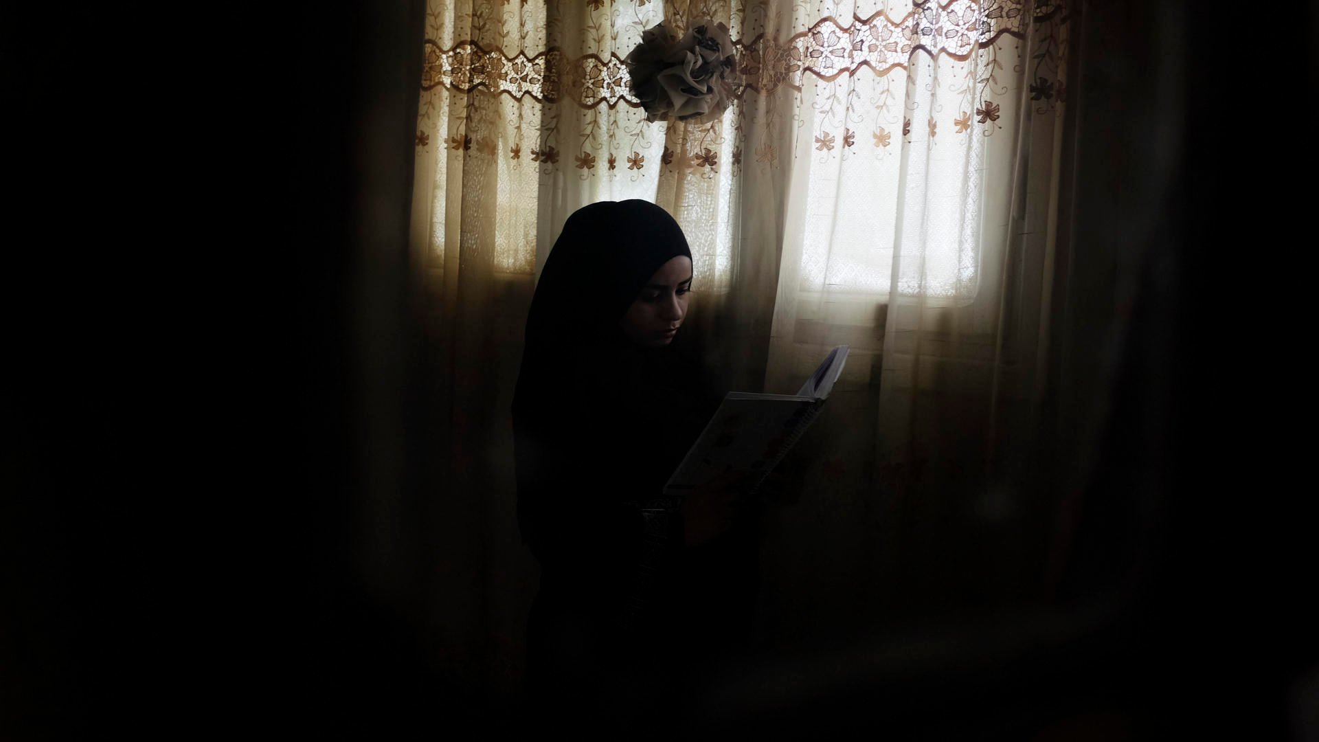 Rawan sits by a window, reading