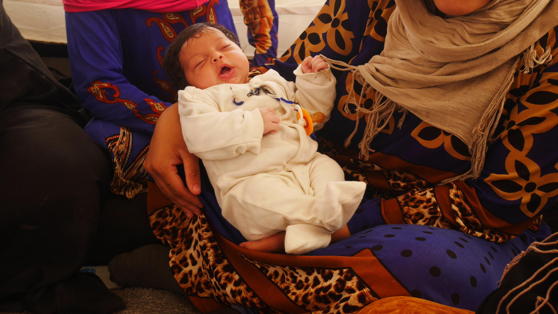Three-week-old baby Ihab in his mother's arms inside a refugee tent