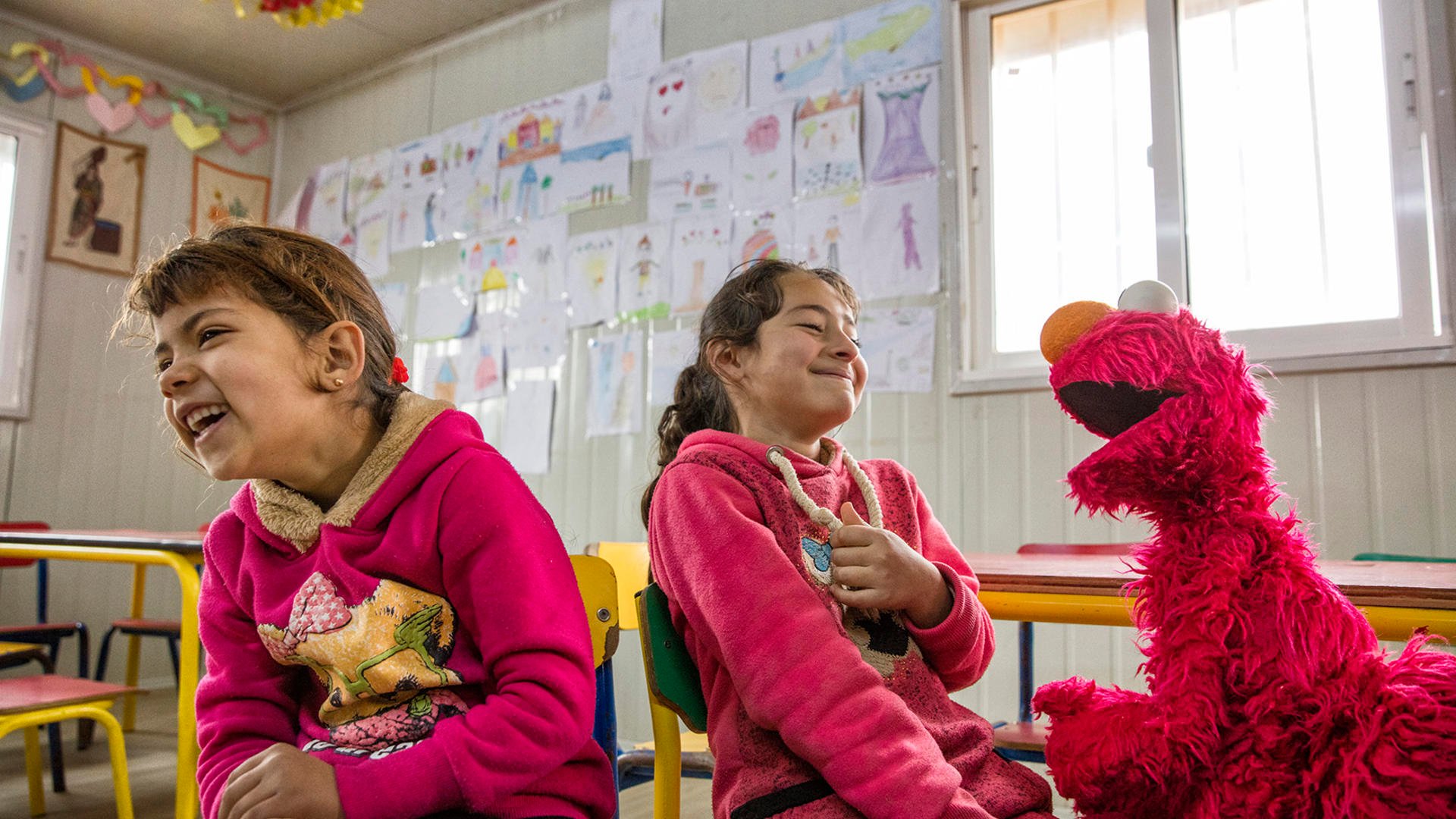 Elmo, the Sesame Street Muppet, makes two Syrian refugee girls laugh