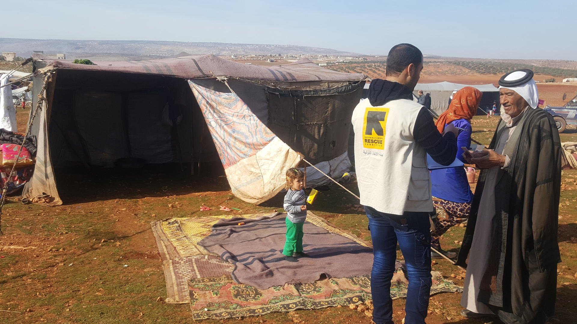 An aid worker speaks with a displaced Syrian man outside his family's tent