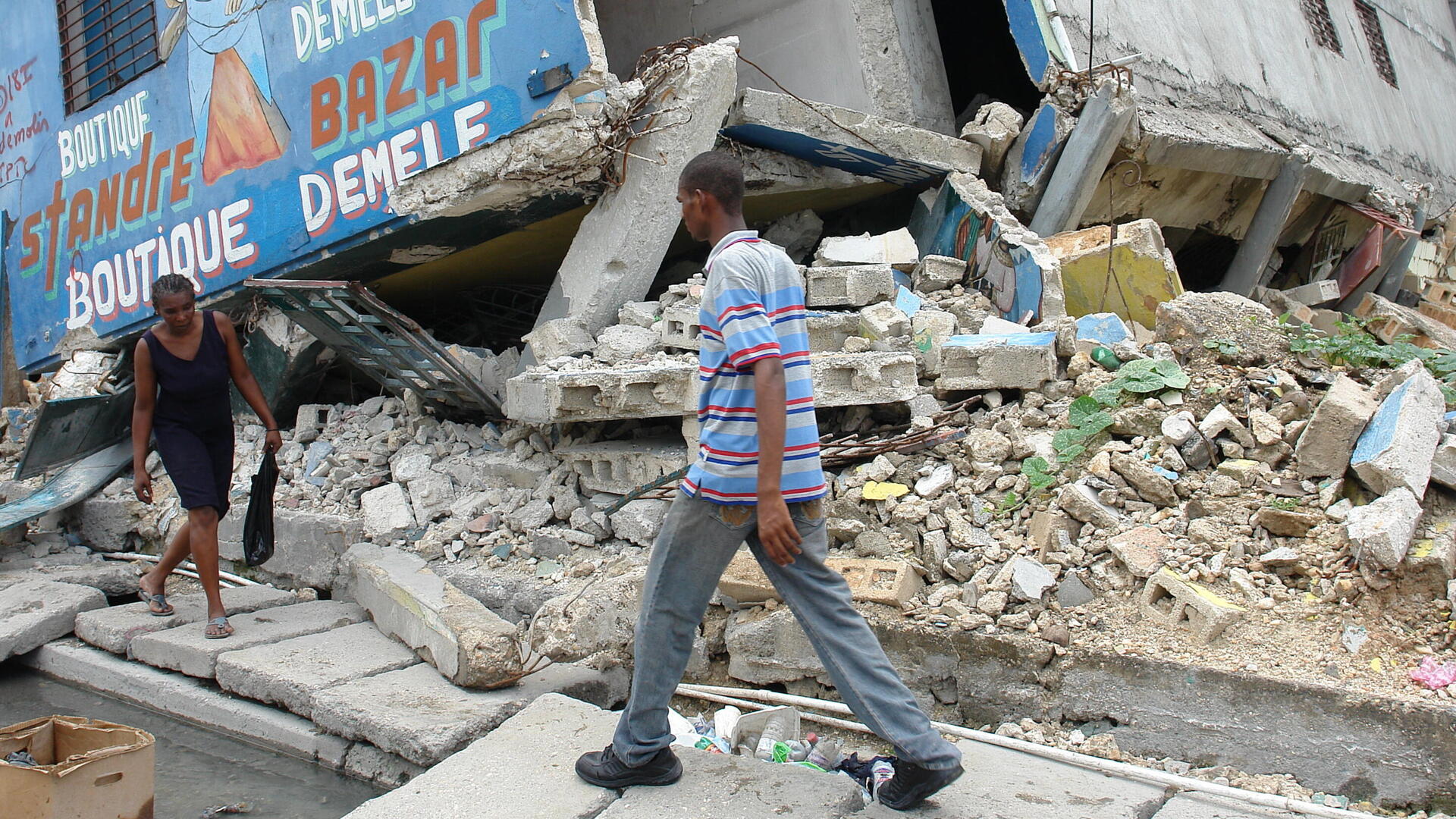 A man and woman walk gingerly past the rubble of buildings in Port-au-Prince, Haiti destroyed by the powerful 2010 earthquake. 