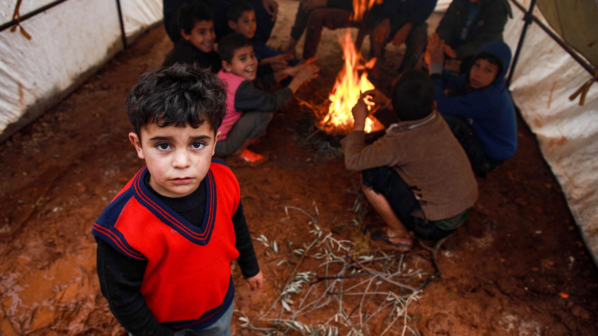 A boy looks on as other children behind sit by a fire inside a tent at a flooded camp for displaced Syrians near the village of Killi in the north of the northwestern Idlib province on December 5, 2019. (Photo by Aaref WATAD / AFP) (Photo by AAREF WATAD/A