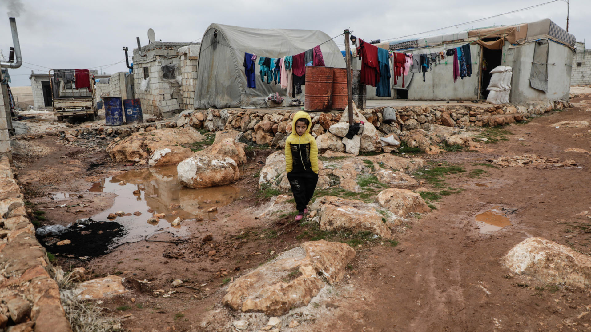 A Syrian boy walks across muddy ground at a settlement for displaced families in Idlib A Syrian boy walks across muddy ground amid tents in Idlib