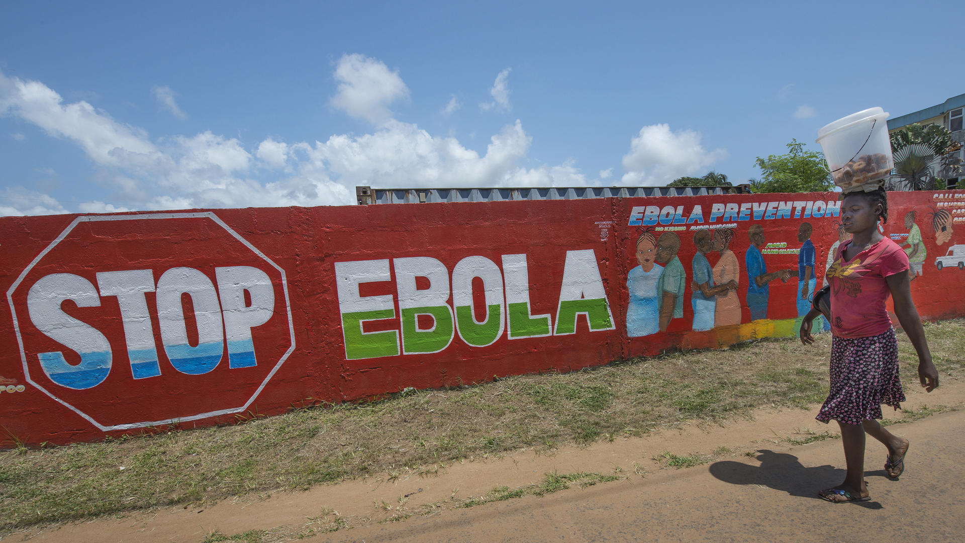 The IRC was at the forefront of efforts to stem the spread of Ebola in West Africa. Photo: Peter Biro A woman in Monrovia, Liberia, walks past a mural that reads "Stop Ebola."