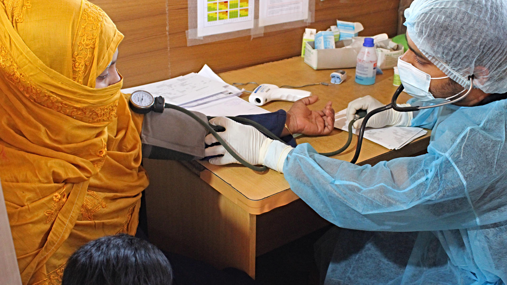An IRC paramedic takes the blood pressure reading of a young woman in Bangladesh as he screens for the coronavirus