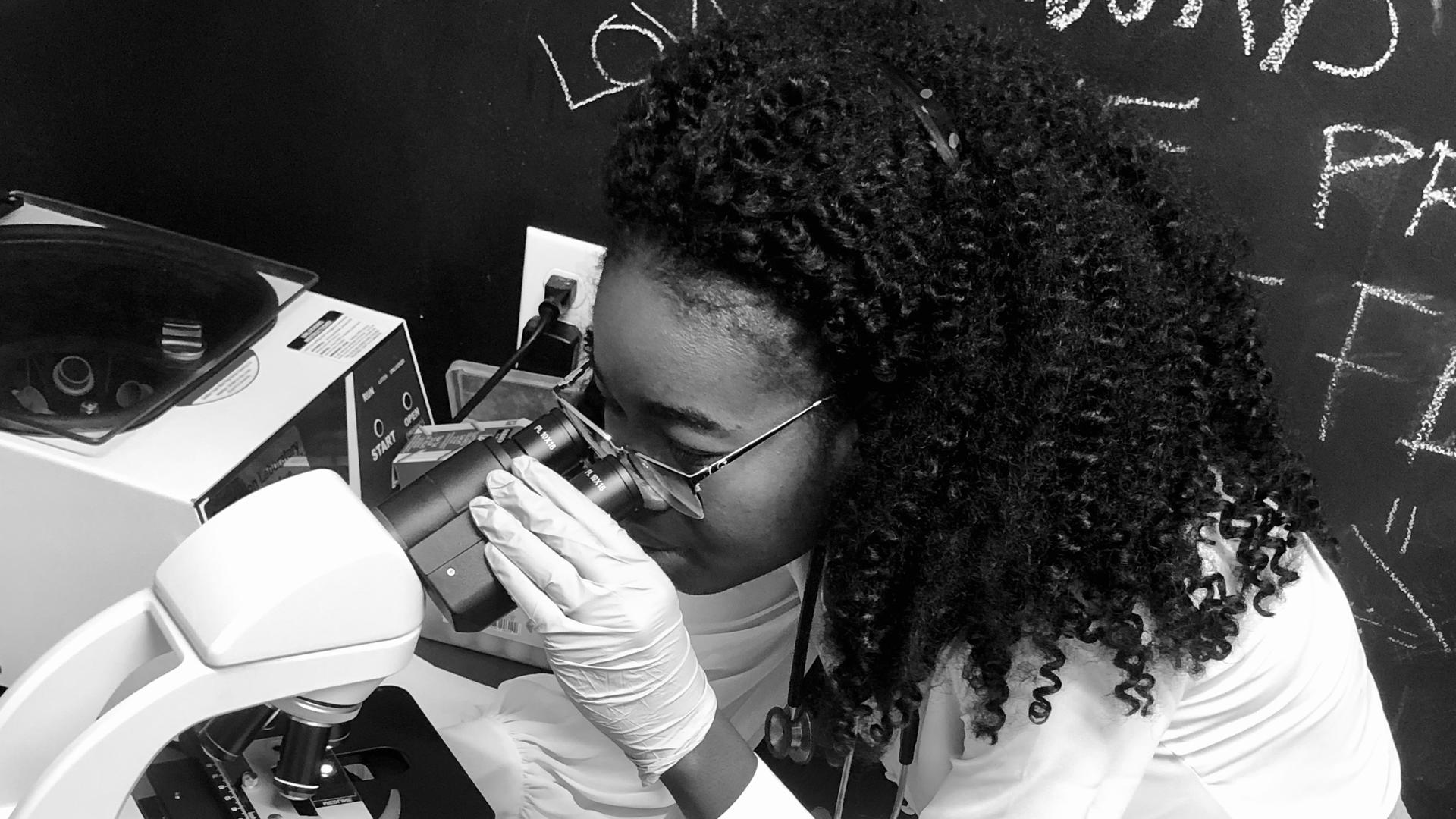 Torbertha Torbor, a nurse practitioner, looks into a microscope