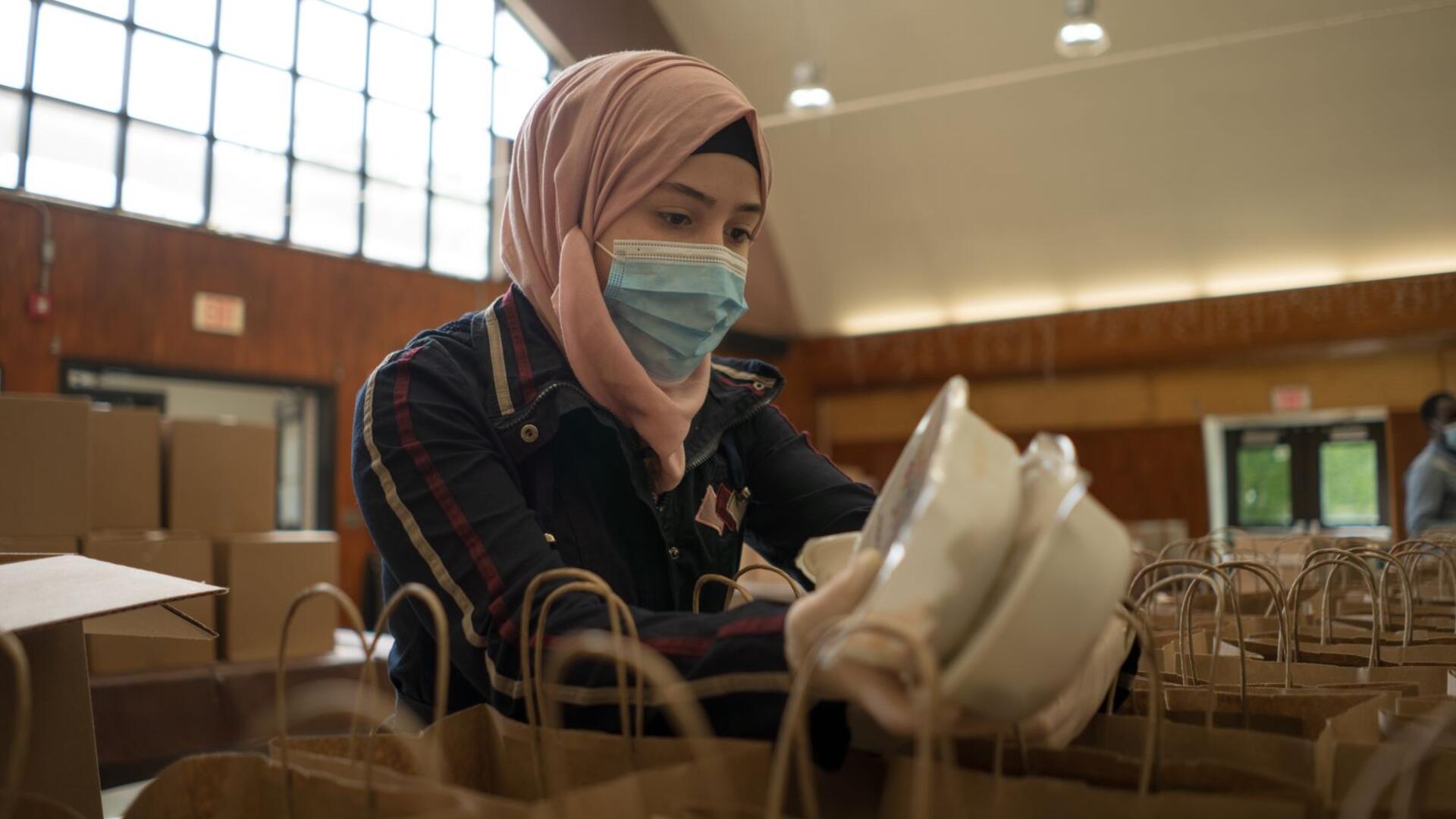 Rania Abou, wearing a mask, puts two containers of food inside paper bags to be given away as part of her work with the IRC and World Central Kitchen.