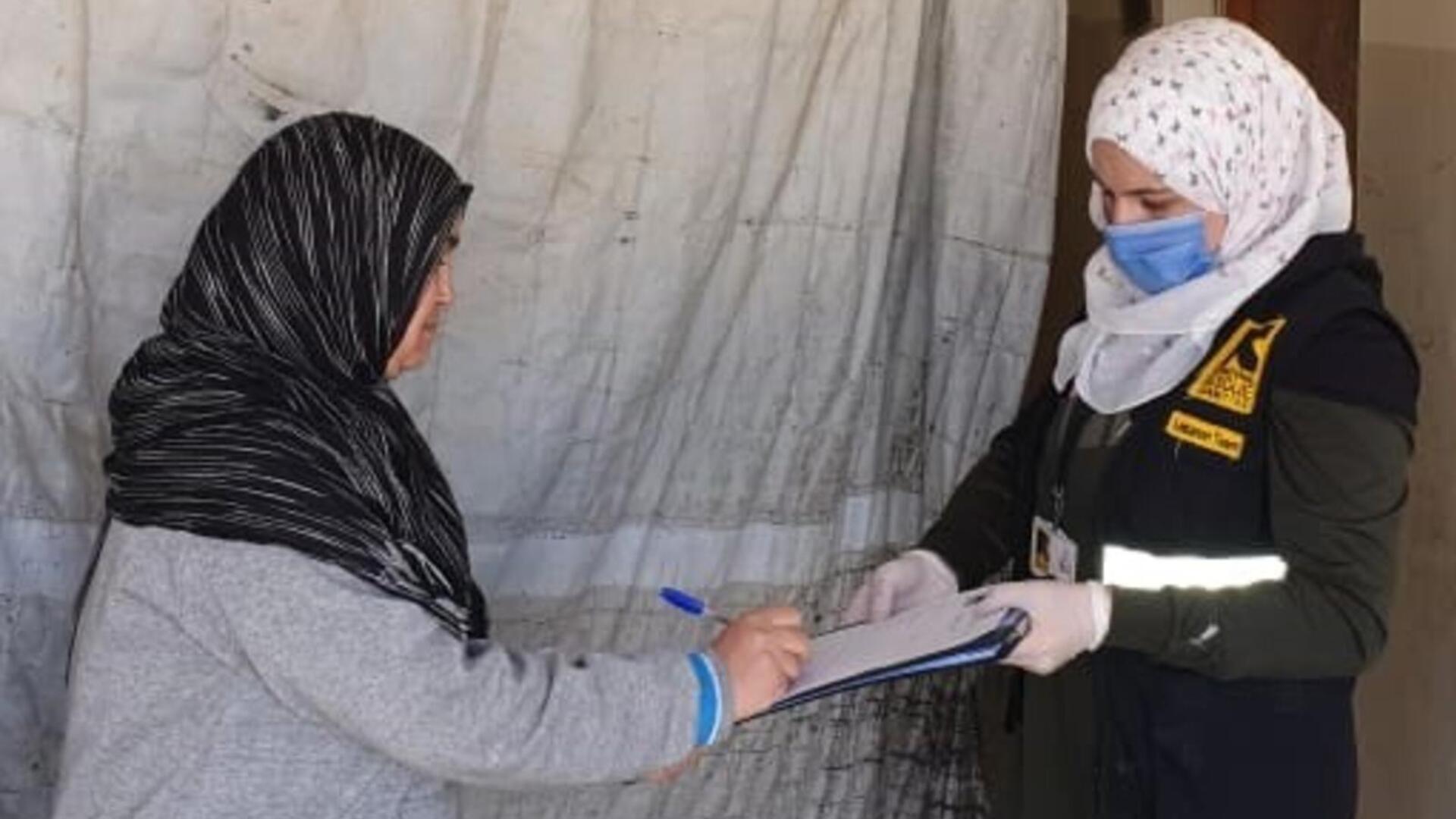 While taking precautionary measures to protect both themselves and others from COVID-19, the IRC distributes emergency cash assistance to vulnerable refugees and people in need across the north Bekaa in Lebanon. A Syrian refugee woman in Labanon signs a form to get cash assistance presented by an IRC staff member wearing PPE.