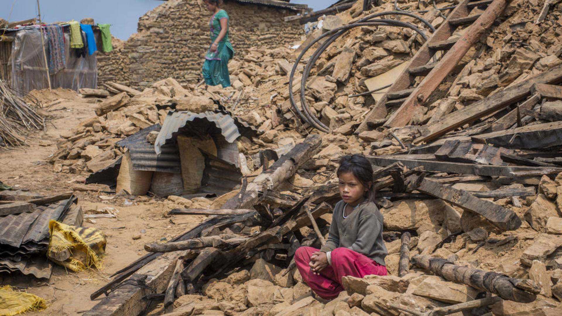 child sits in earthquake rubble in Nepal