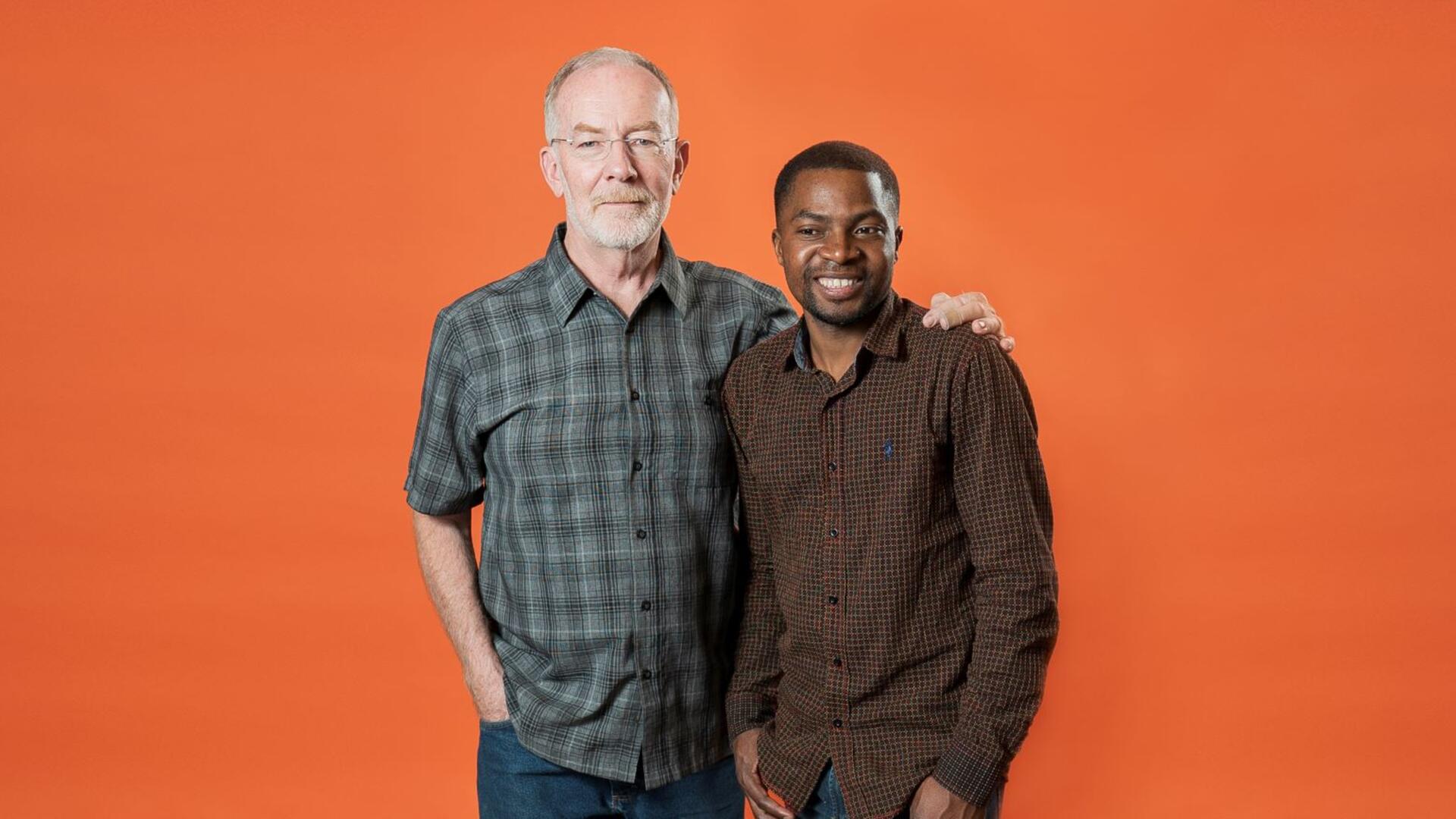 Robert Sebatware and Dave Kurz posing for the camera in front of an orange background. 
