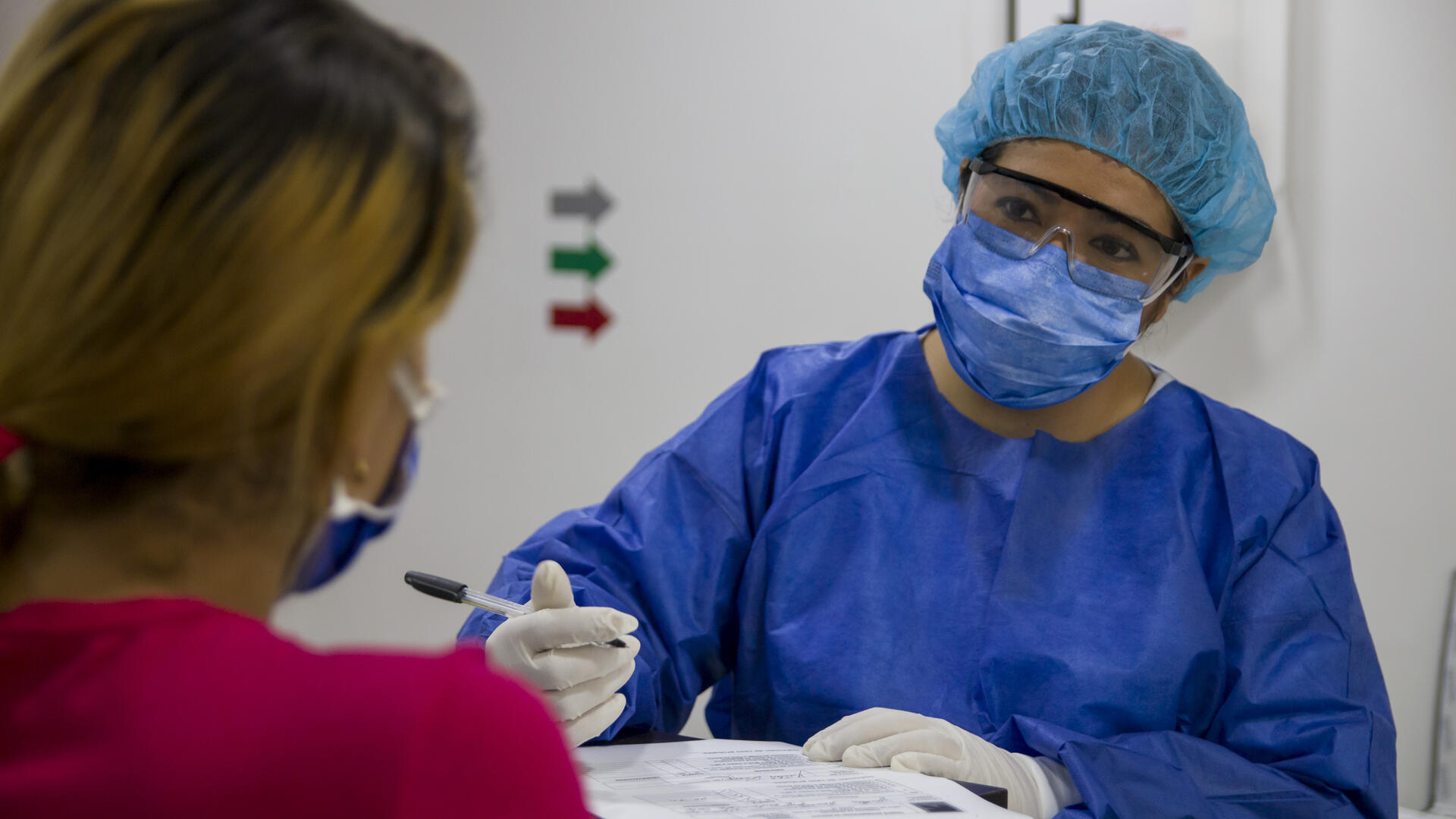 A health worker wearing a face mask and other equipment to protect herself from COVID-19 speaks with an incoming patient at an IRC clinic in Colombia during the pandemic.
