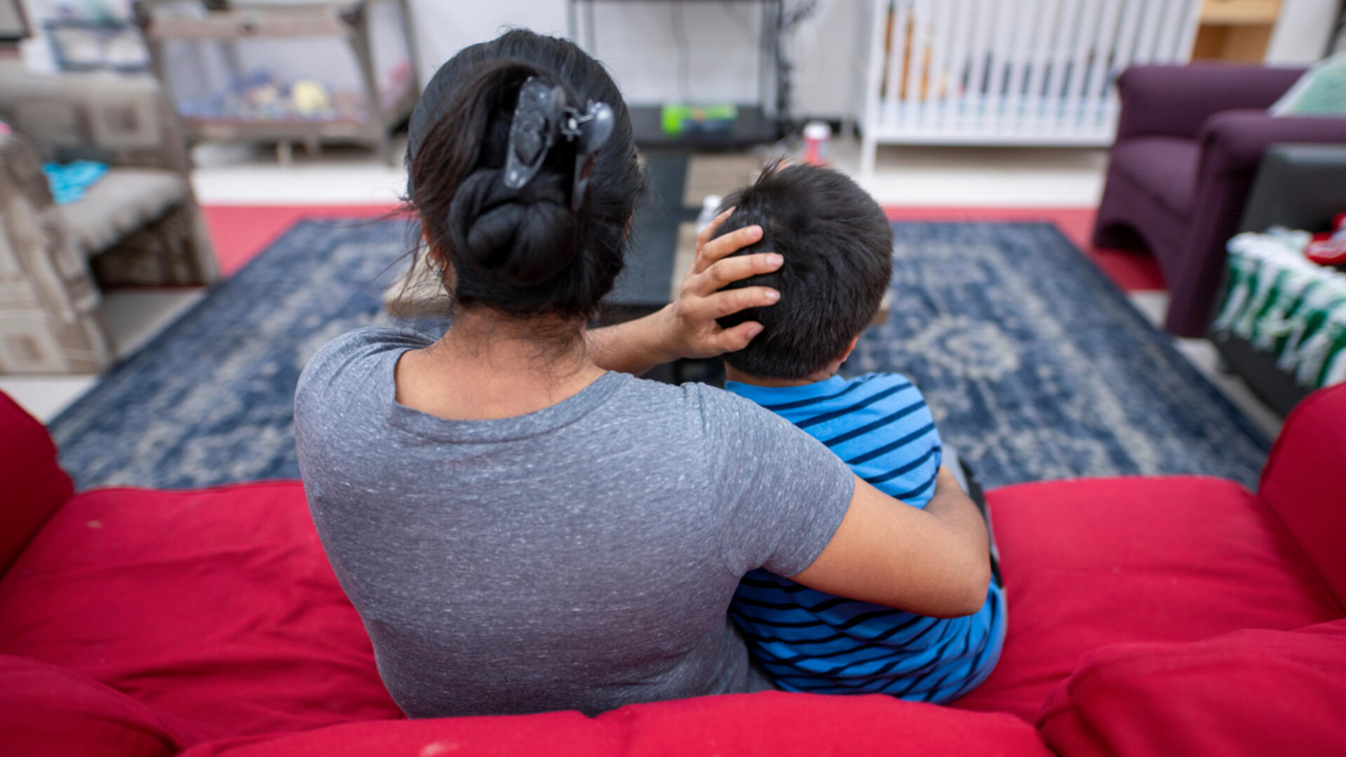 Angelina, an asylum seeker from Guatemala, sits on a red couch with her arms around her son at an IRC Welcome Center in Arizona. 