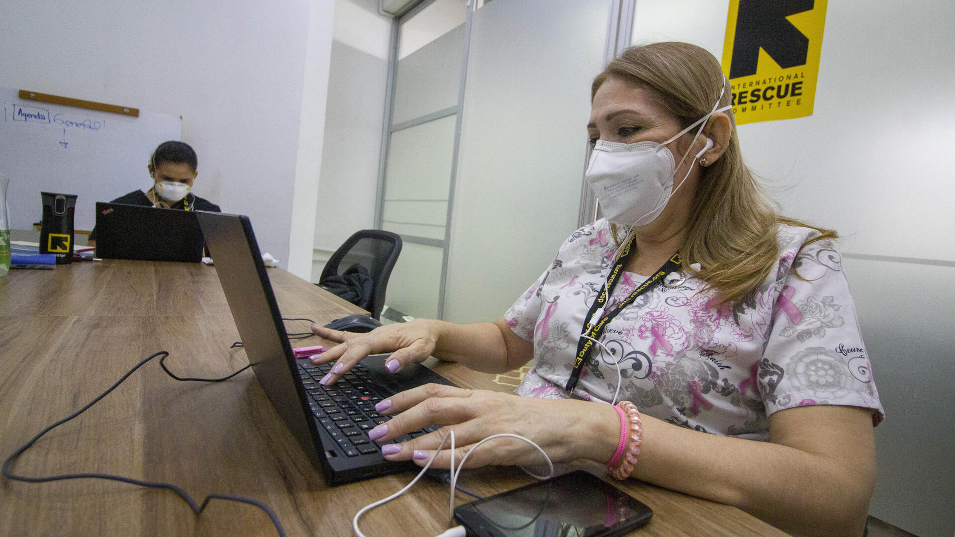 An IRC healthworker wearing a mask to protect herself from COVID-19 types at a laptop
