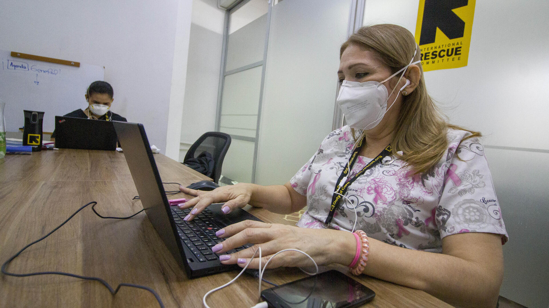 The IRC is using innovative solutions to protect people around the world from the worst impacts of the COVID-19 crisis. An IRC healthworker wearing a mask to protect herself from COVID-19 types at a laptop