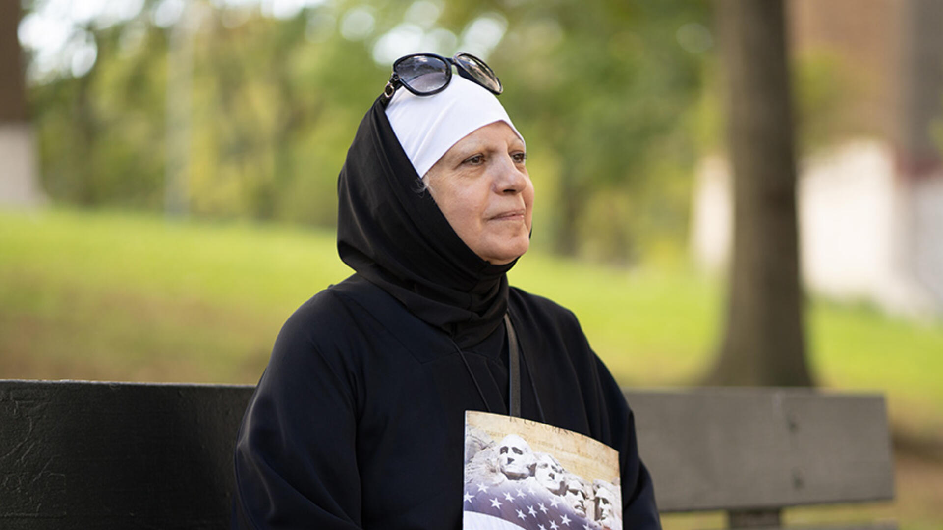 Maha al-Obaidi, a refugee from Iraq whose family was blocked by Trump Administration policies Maha al-Obaidi sits on a park bench looking off into the distance and holding a U.S. citizenship test study book.